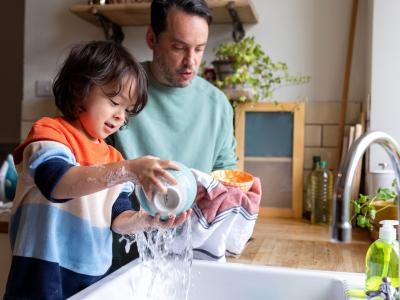 A man and young child wash dishes together